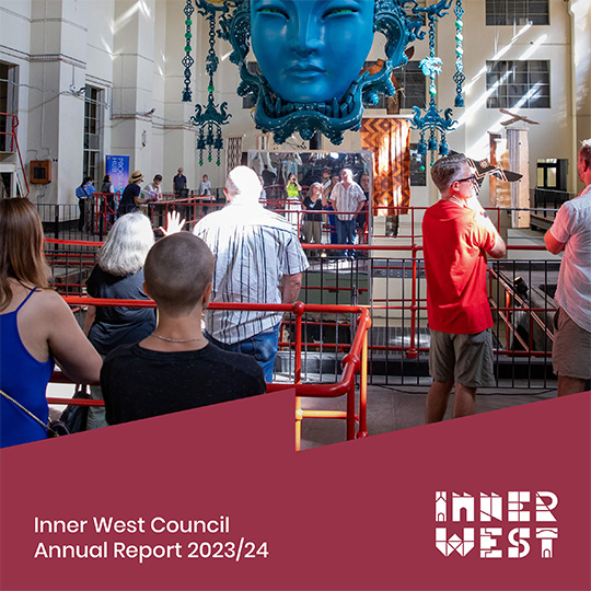 An exhibit in a repurposed industrial building. In the cnetre of the room is a sculpture of a large ornately-decorated blue head suspended from the ceiling. Text overlay saying 'Inner West Council Annual report 2023/24'